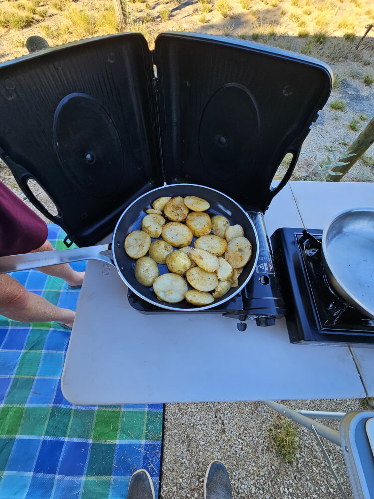 My Famous Potatoes Sliced potatoes frying in a pan on a portable butane cooker