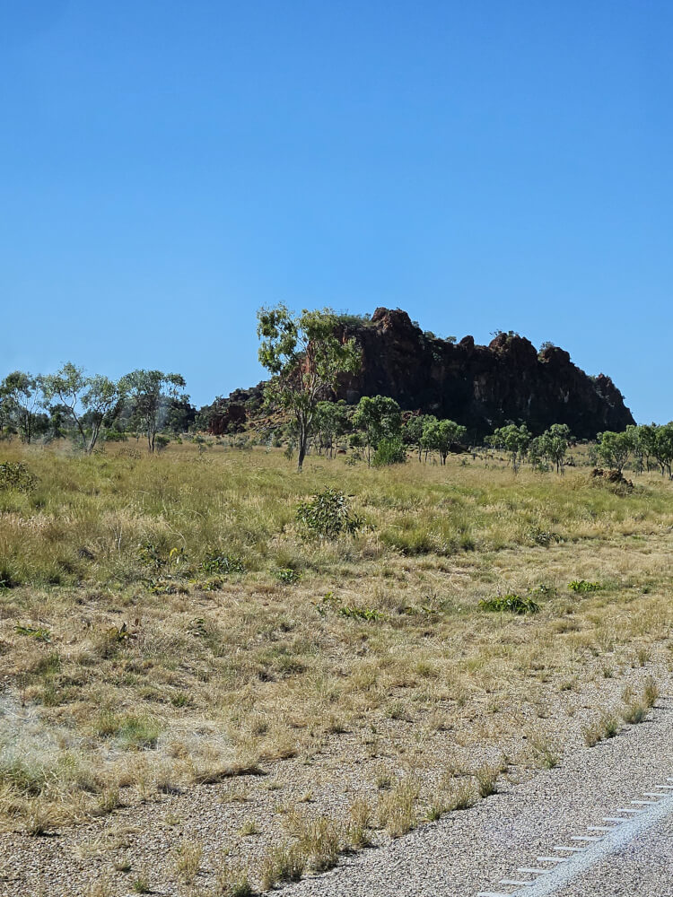 Kimberley Rock Country Large dark rock formation rising from grassland beside the highway