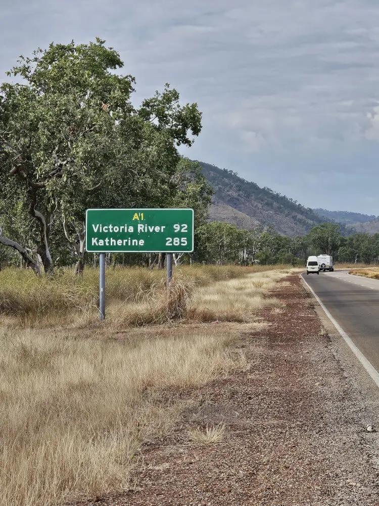 Road sign beside the Victoria Highway near Timber Creek, with trees and rocky hills in the background.