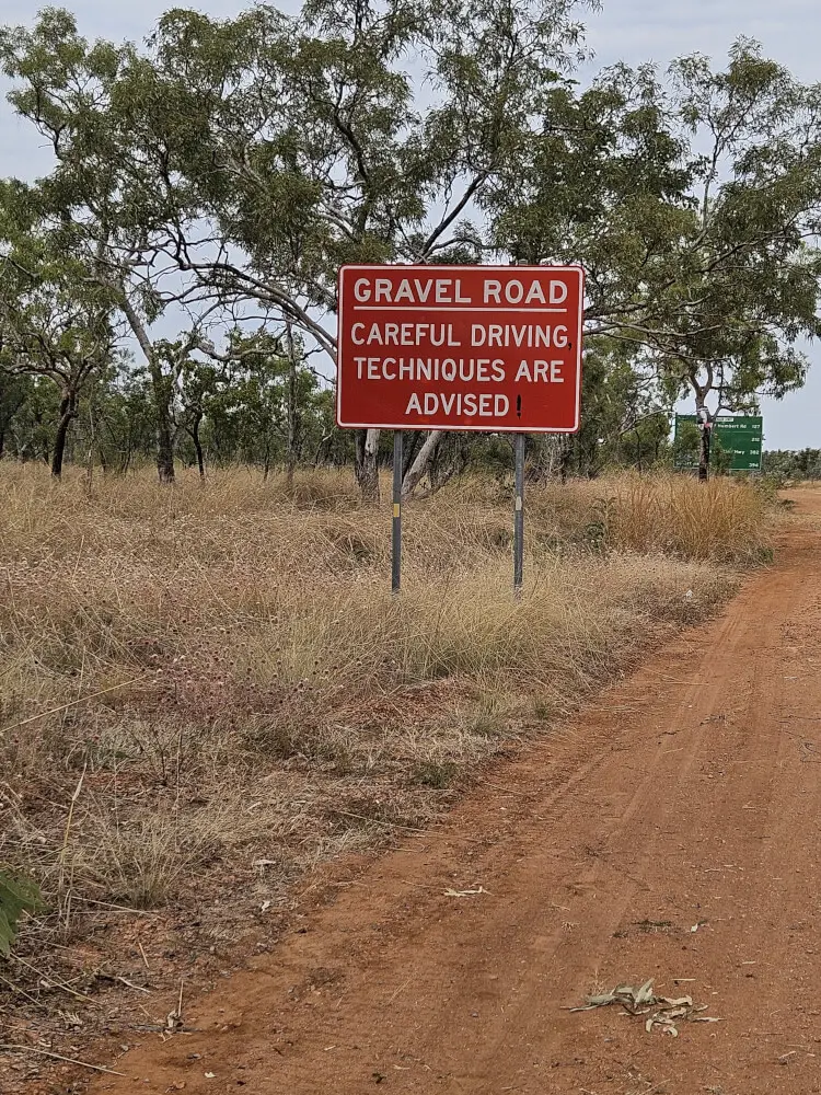 Gravel Road Warning Sign | Victoria Highway, NT Red warning sign advising motorists of gravel road conditions on a dirt road off the Victoria Highway in the Northern Territory.